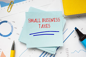 Note with 'Small Business Taxes' on a desk with financial documents and a pen.